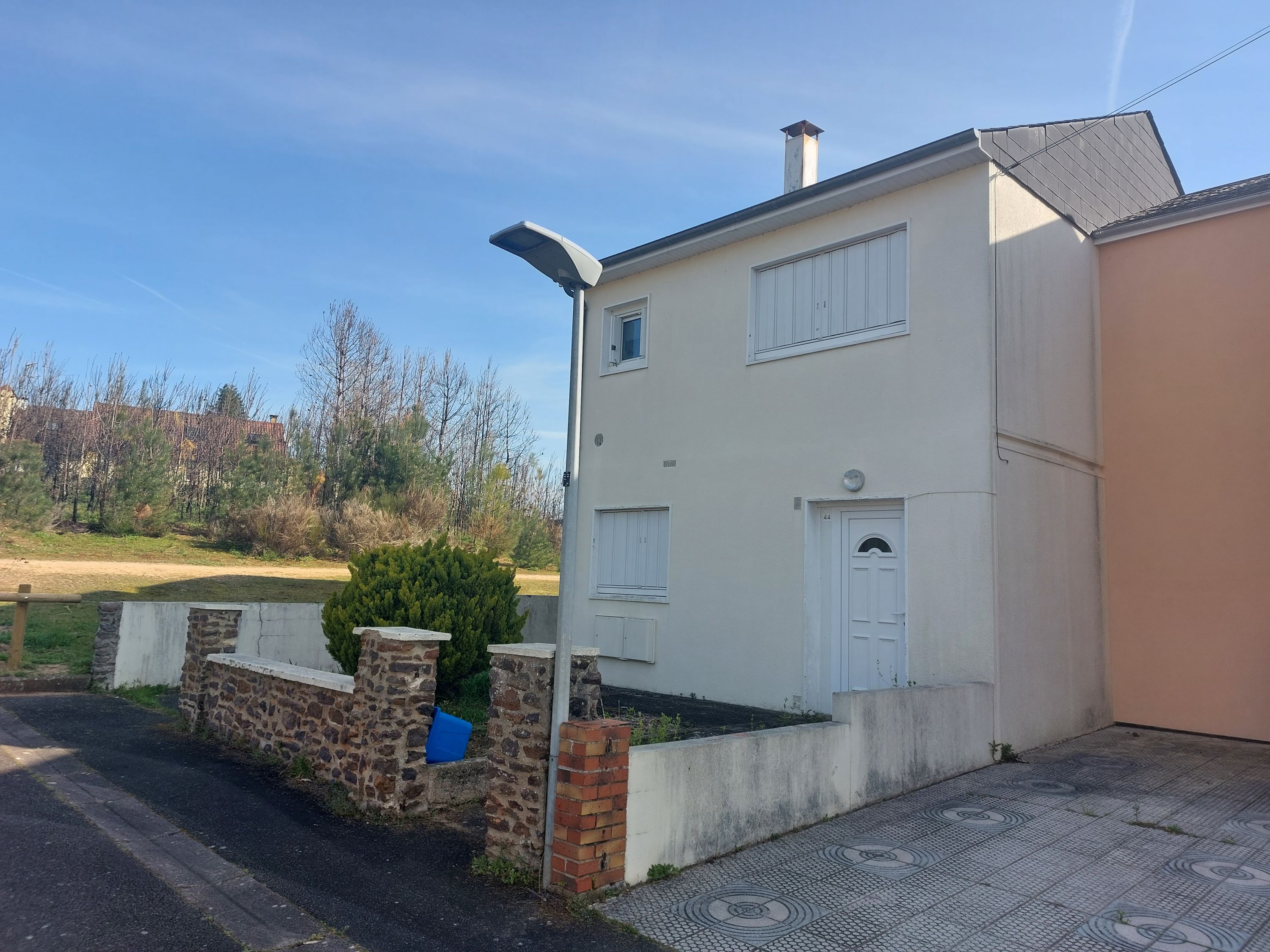 Vue de face d'une maison semi-mitoyenne avec un étage et un petit jardinet sur le devant. Muret en pierre et façade blanche, bien entretenue.